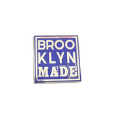Enamel pin with 'BROOKLYN MADE' text on a wooden surface with a dark purple background