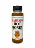 Bottle of Harissa Hot Honey with a wooden honey dipper on a wooden surface.