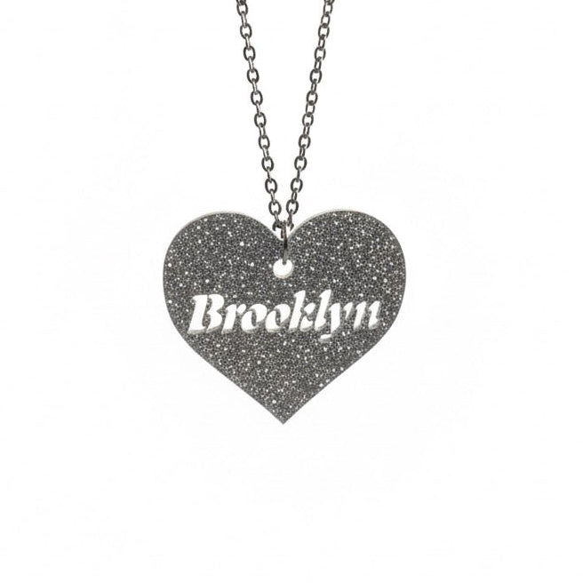 Heart-shaped pendant with 'Brooklyn' engraving on a chain against a white background