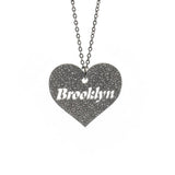 Heart-shaped pendant with 'Brooklyn' engraving on a chain against a white background
