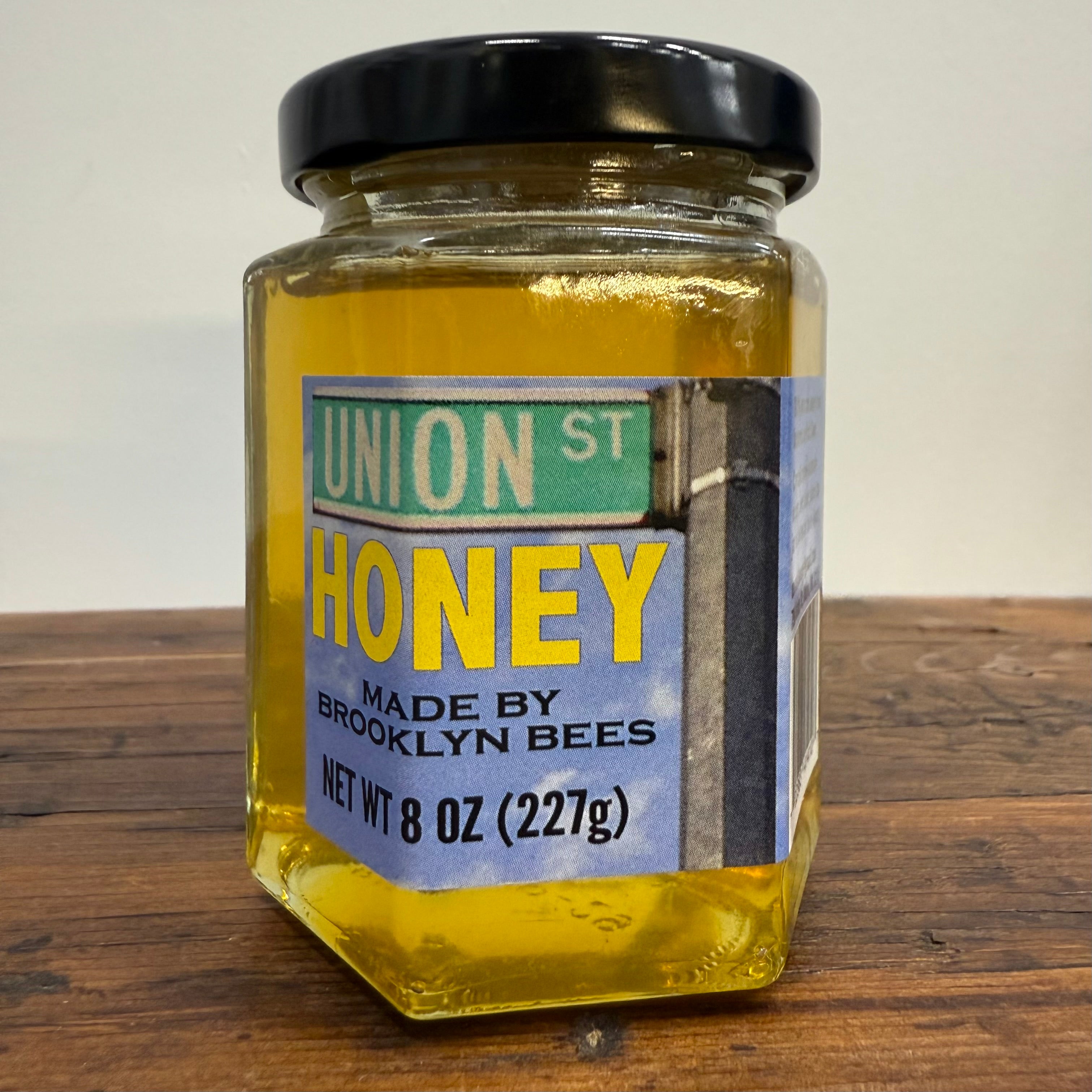 Jar of honey with a label reading 'Union St Honey Made by Brooklyn Bees' on a wooden surface.