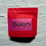 Red packaging with a pink label featuring buddies on a gray textured background whole bean medium to dark roast 
