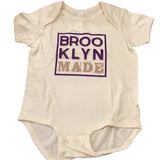 A white onesie with 'Brooklyn Made' printed in purple text on the front.