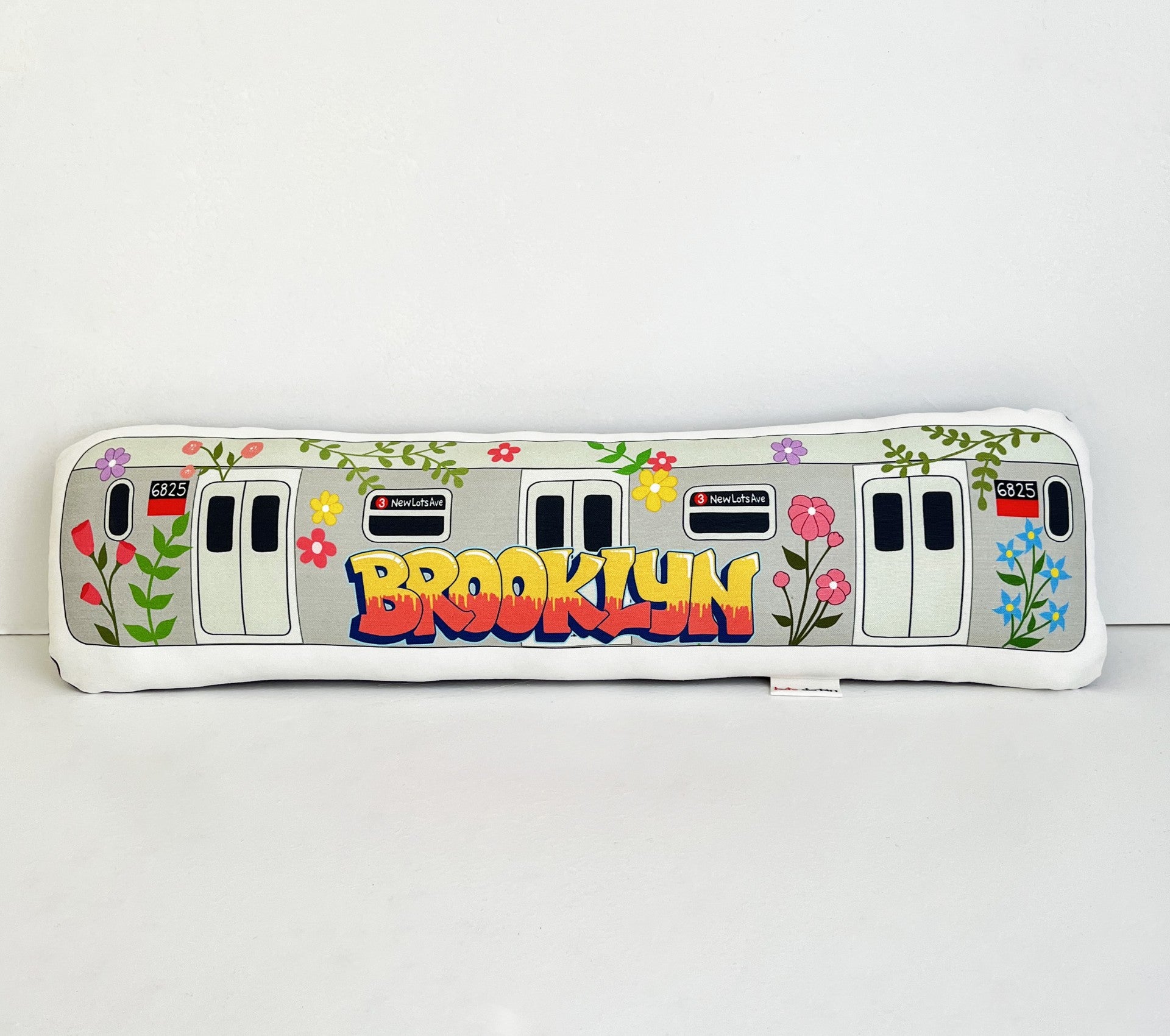 Decorative pillow shaped like a subway car with 'Brooklyn' text and floral designs on a white background