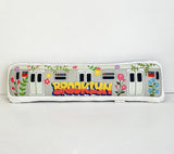 Decorative pillow shaped like a subway car with 'Brooklyn' text and floral designs on a white background