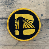 Black and gold patch with a logo on a wooden surface