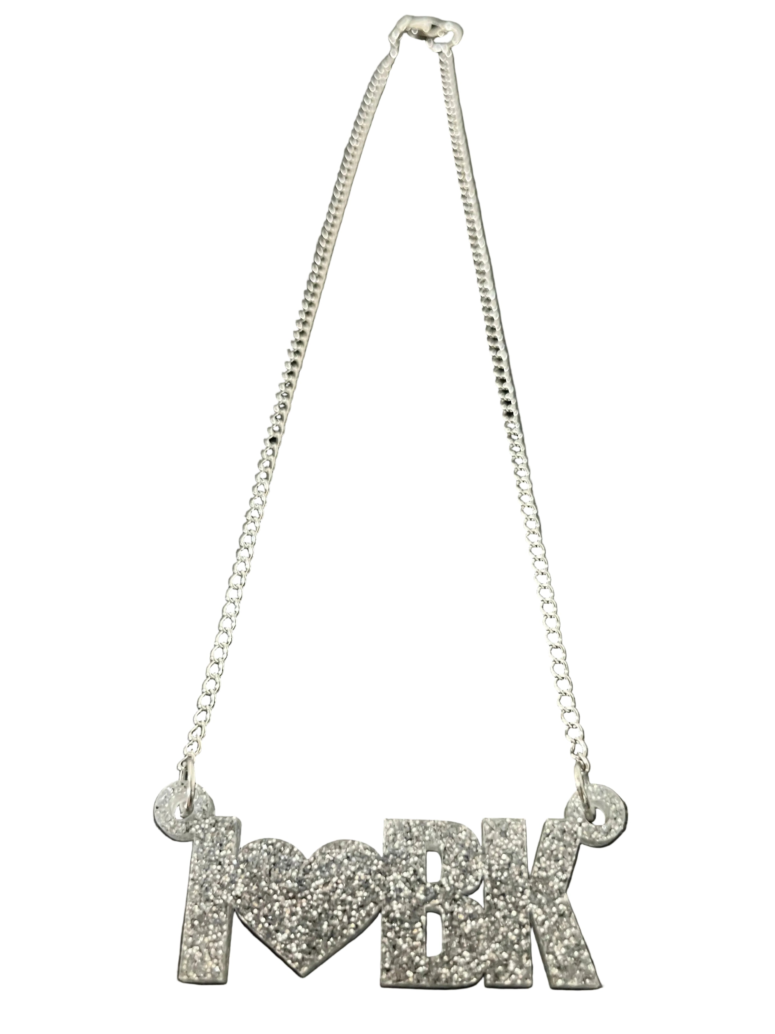 Silver necklace with 'I heart BK' pendant on a dark wooden surface