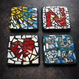 Four square mosaic coasters with colorful patterns on a dark surface