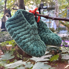 Green knitted slippers hanging on a branch with a blurred natural background