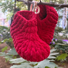 Red knitted slippers hanging on a branch with a natural background