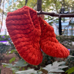 orange knitted slippers hanging on a tree branch with a natural background