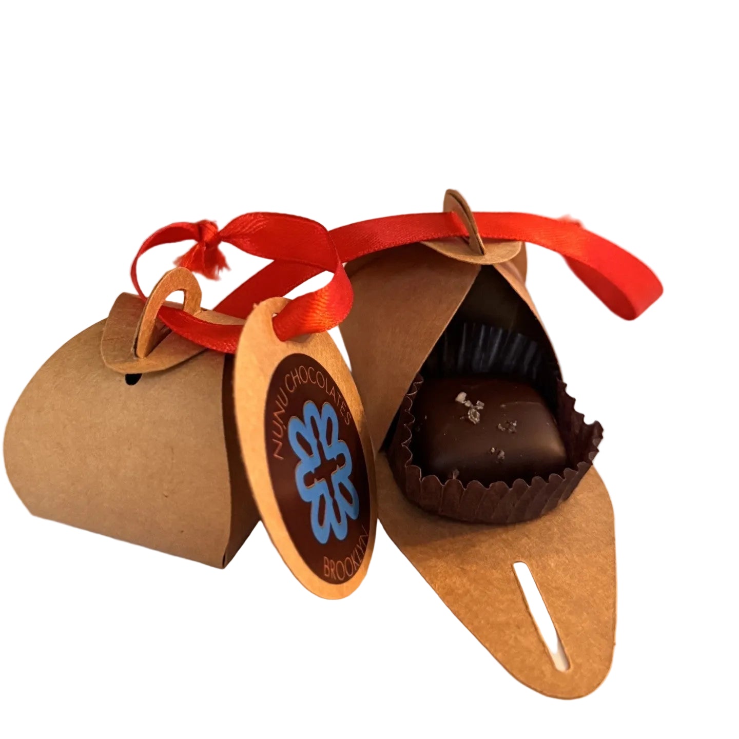 Chocolate treat in a brown paper packaging with a red ribbon, set against a Christmas tree branch background.